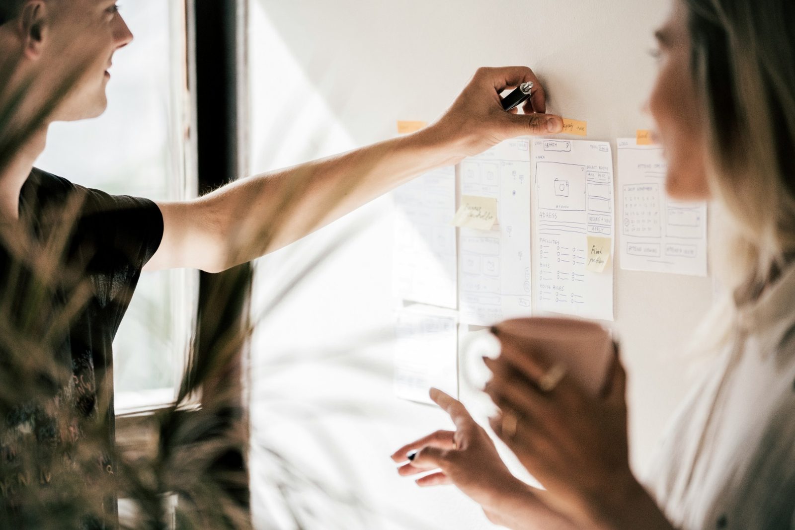 Two colleagues mapping out a plan with sketches and sticky notes on a wall
