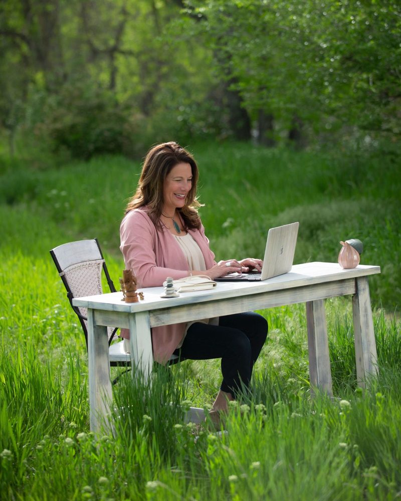 Tiffany Edgar laughing as she works on a laptop at a desk in a meadow