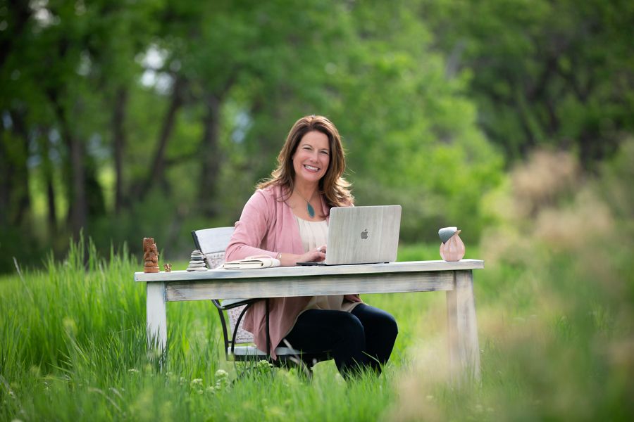 Tiffany Edgar smiling at her laptop at a desk in a Colorado meadow