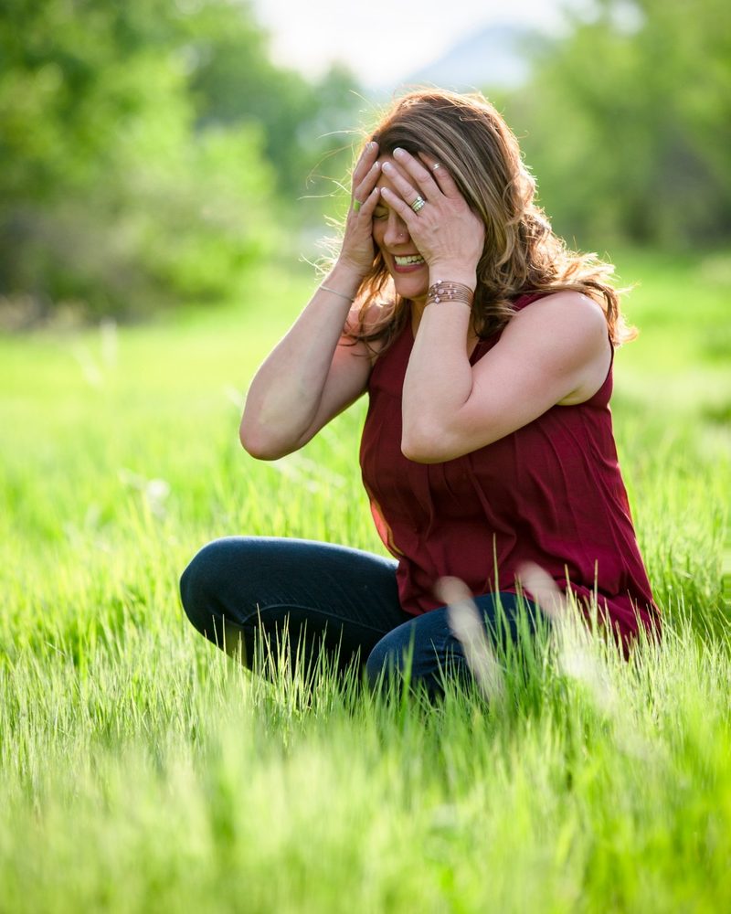 Tiffany Edgar sitting in tall grass, laughing with her hands on her head