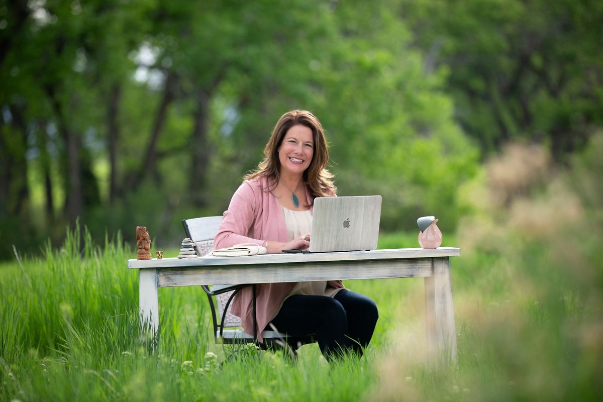 Tiffany Edgar smiling at her laptop at a desk in a meadow